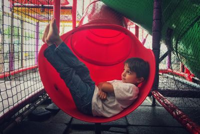 Side view of thoughtful boy lying on slide at playground