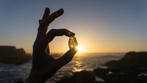 Cropped hand holding gemstone at beach during sunset