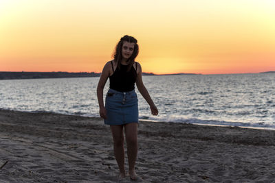 Full length portrait of woman standing on beach during sunset