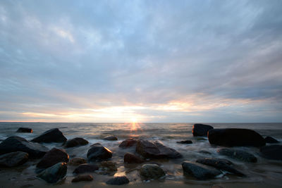 Rocks on beach against sky during sunset