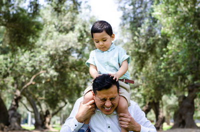 Father carrying son on shoulders against trees in park