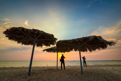 Silhouette people on beach against sky during sunset