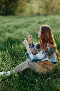 Rear view of woman using mobile phone while sitting on grassy field