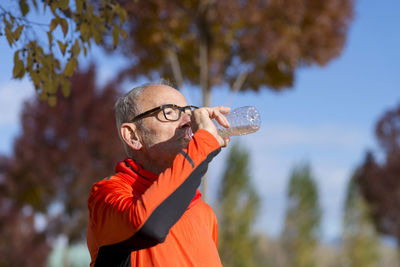 Senior man drinking water while standing at park