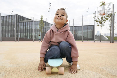 Smiling boy sitting on skateboard at sports field