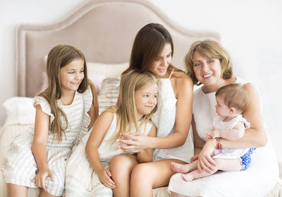 Cheerful mothers with kids sitting on bed at home