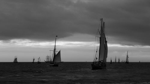 Sailboats sailing in sea against cloudy sky