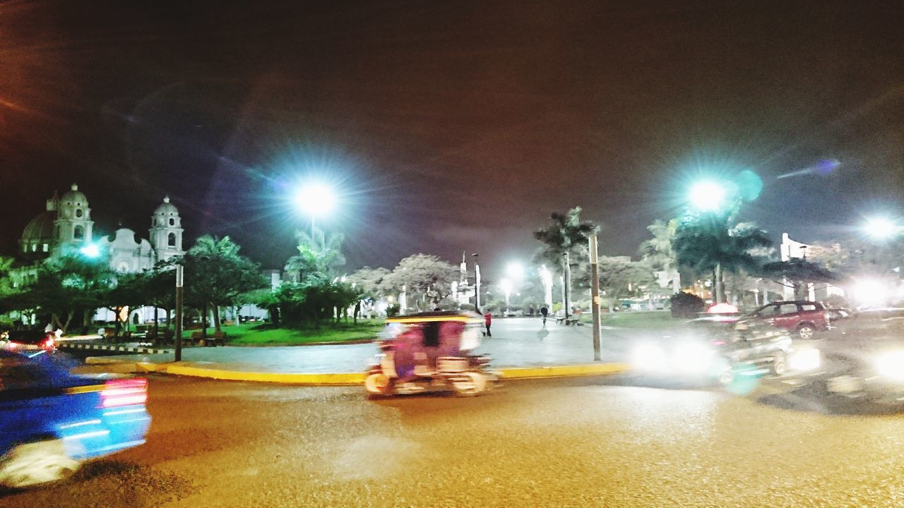 illuminated, night, lens flare, glowing, blurred motion, light beam, speed, long exposure, street, land vehicle, transportation, large group of people, street light, motion, real people, road, outdoors, carousel, city