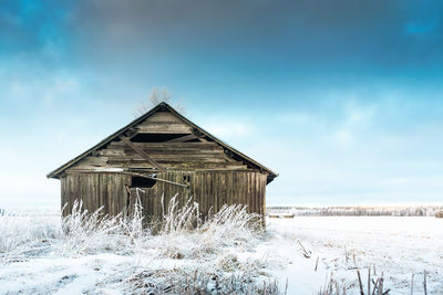 Abandoned barn on snow covered field against sky