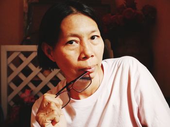 Close-up portrait of mature woman holding eyeglasses while sitting at home