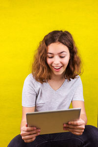 Smiling young woman using mobile phone against yellow wall