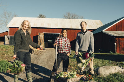 Portrait of male and female farmers with organic vegetables standing outside barn