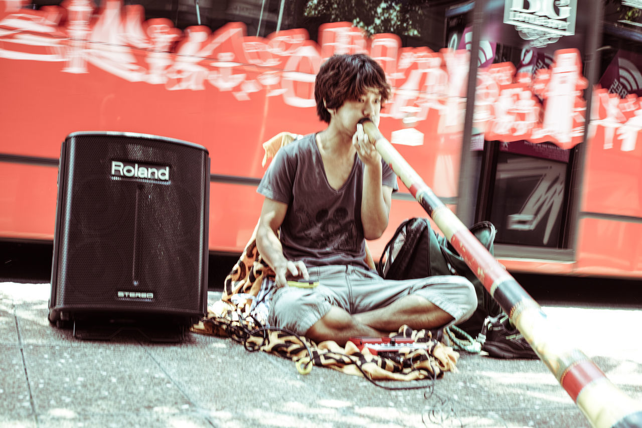 FULL LENGTH OF MAN SITTING ON STREET AGAINST CITY