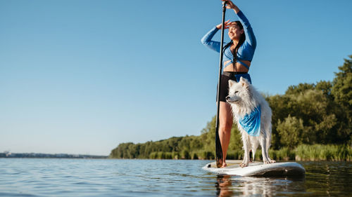 Woman enjoying life on the lake at early morning standing on the sup board with dog japanese spitz