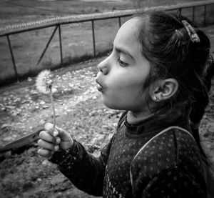 Side view of girl blowing dandelion on field