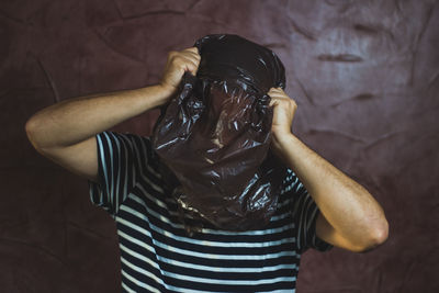 Man with face covered by plastic bag against wall