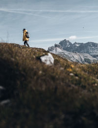 Man hiking in the dolomites on a gras plateau with a senic view of mountain tops and clear sky