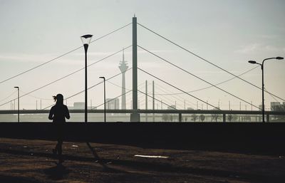 Silhouette man walking on footpath against sky in city