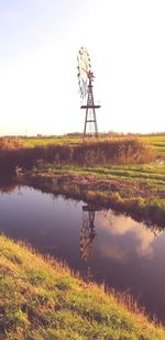 Windmill on field by lake against sky