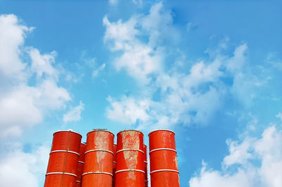 Low angle view of mixed concrete tanks against blue cloudy sky