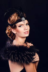 Elegant young woman in black lingerie with fur boa posing at studio on black background