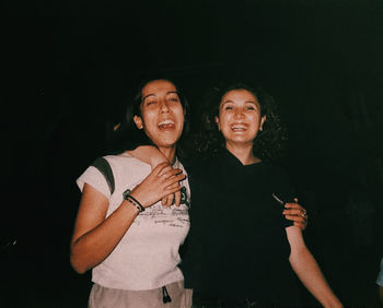 Portrait of happy friends standing against black background