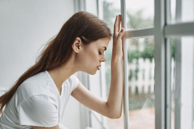 Portrait of young woman looking away while standing against window