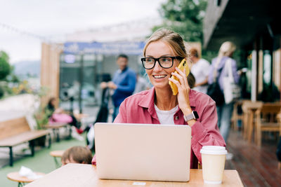 Young blonde business woman sitting on the terrace in a cafe working on a laptop.