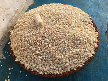 A basket on a blue floor full of kernels of corn and an empty husked corn on top of it 