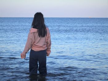 Rear view of young woman standing in sea against sky