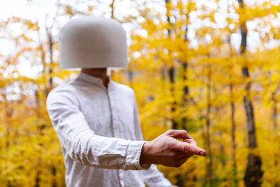 Man wearing bowl on head pointing away against trees