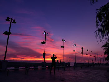 Silhouette people standing on street against orange sky