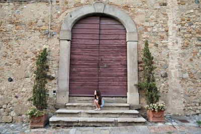 Cute girl sitting on steps outside closed old building door