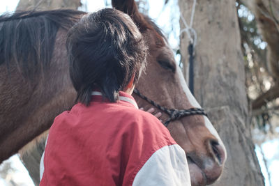 Rear view of boy with horse standing at farm