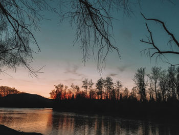 Silhouette trees by lake against sky during sunset