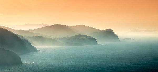 Scenic view of sea and mountains against sky during sunset