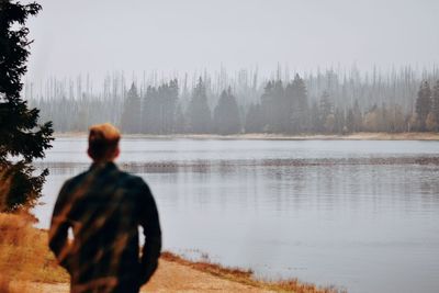 Rear view of man looking at lake against sky