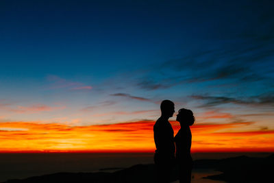 Silhouette couple standing against orange sky