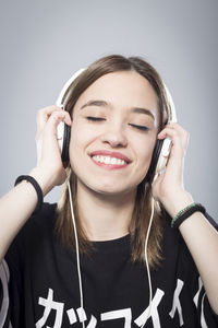 Close-up of young woman listening music on headphones against gray background
