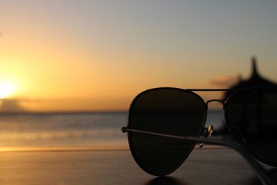 Close-up of sunglasses on beach against sky during sunset