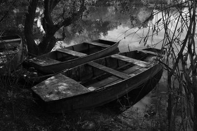 Abandoned boat moored by trees against sky