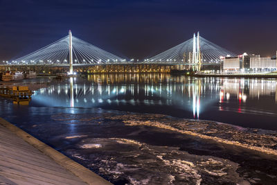 Illuminated bridge and buildings reflecting on river at night