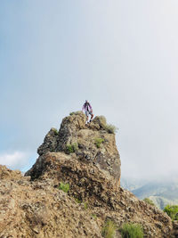 Man climbing rock on mountain against sky