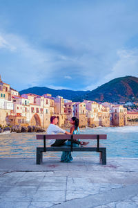 People sitting by buildings against sky in city