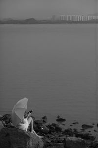 Man sitting on rock by sea against sky