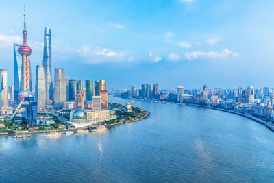 View of city buildings by river against sky