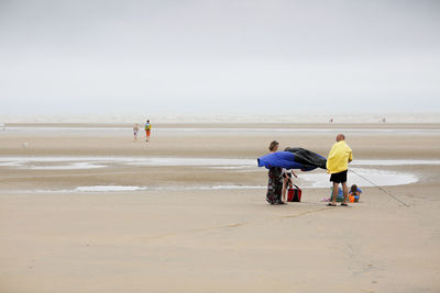 Rear view of men walking on beach against sky