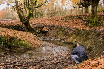 Rear view of man photographing stream in forest