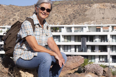 Portrait of smiling senior woman sitting against buildings