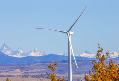 Wind turbines in field against blue sky and mountains